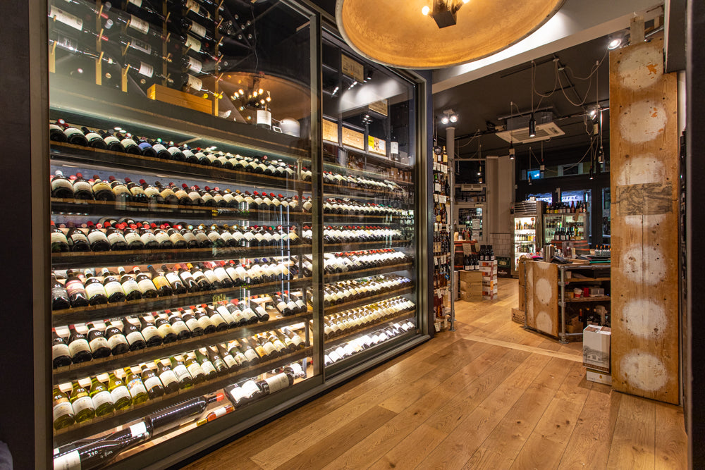 A picture of the fine wine cabinet in the Salusbury Winestore looking into the front of the shop, taken in evening.
